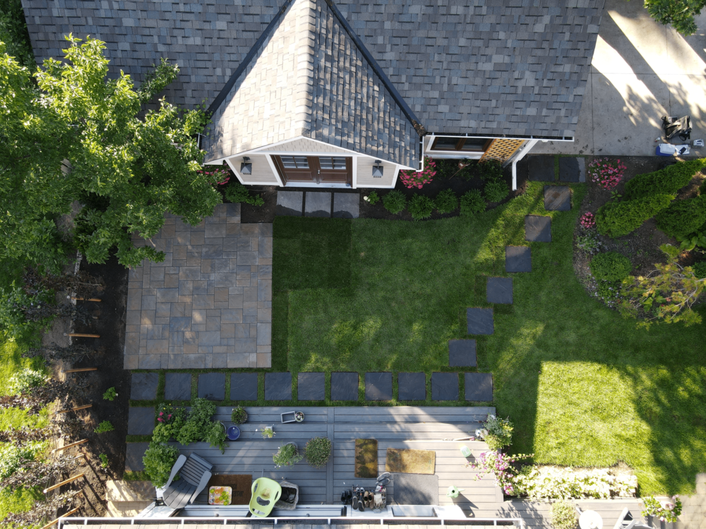 Aerial image of a backyard with a deck, stone slab patio and a stepping stone pathway.