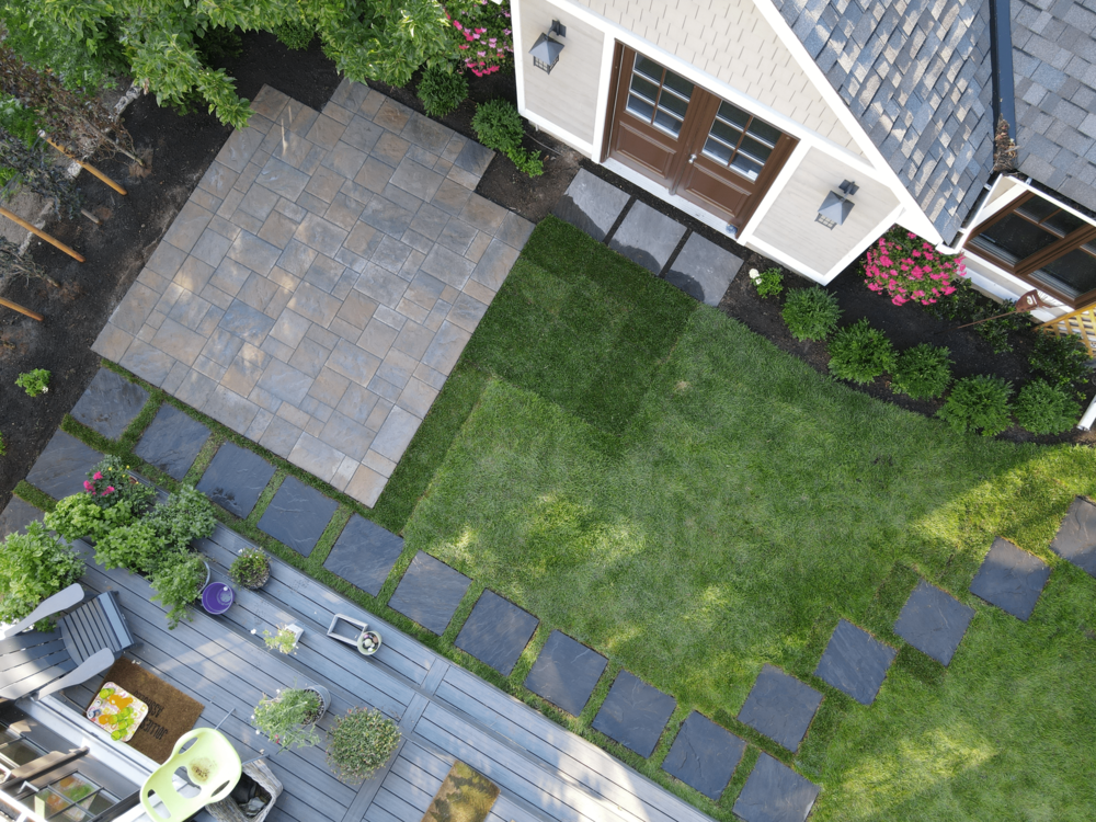 Overhead image of a backyard with a deck, stone slab patio and a stepping stone pathway.